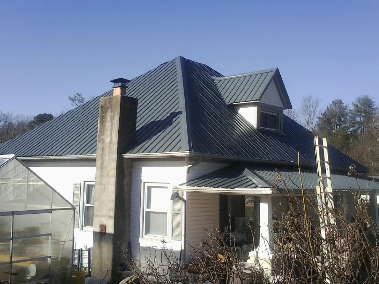 Dark blue standing seam metal roof on a white farmhouse with dormer — Slate & Tile Roof Repair by Roofing Brothers in Kenmore