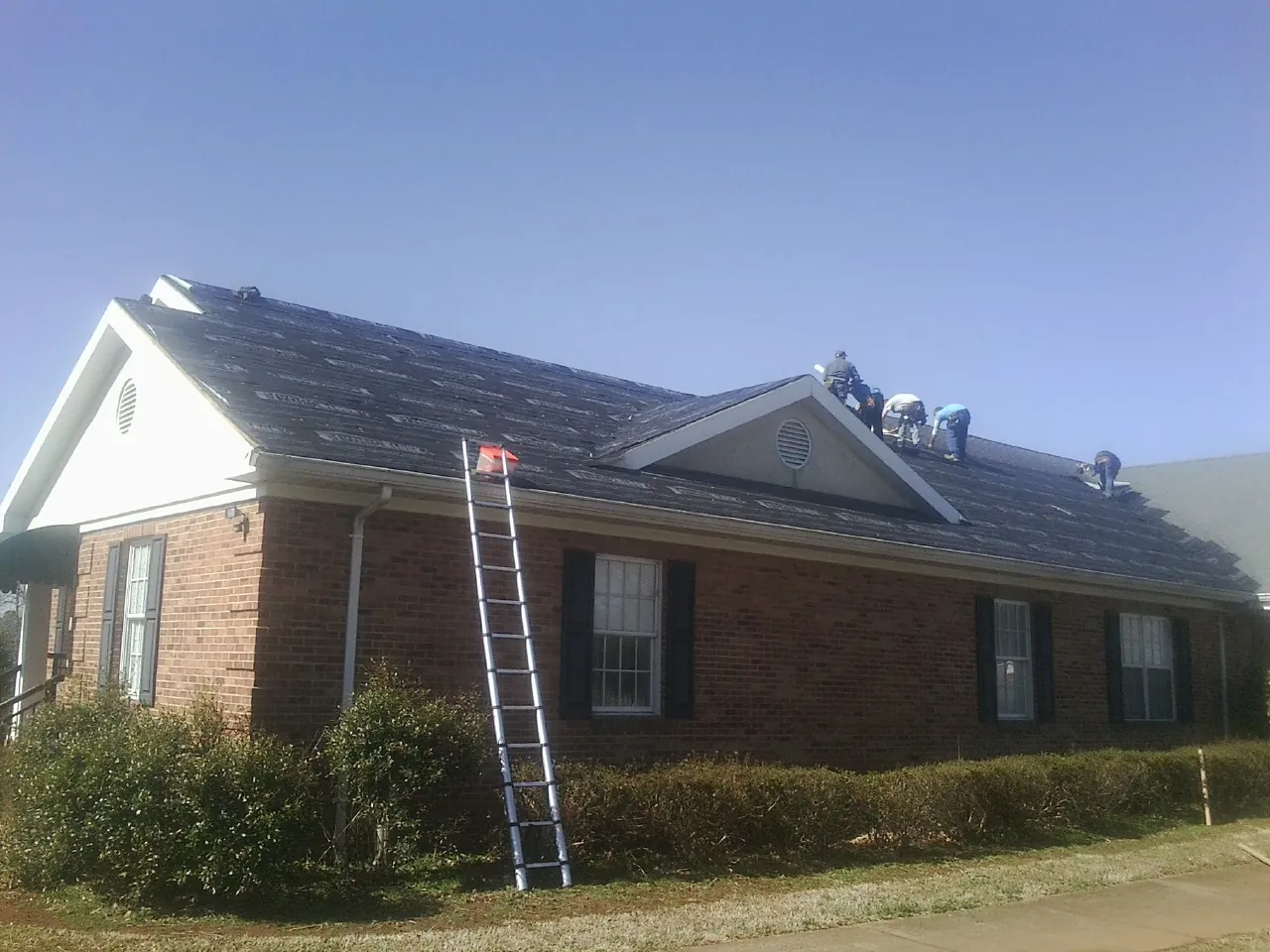 Crew tearing shingles off a brick ranch roof with a ladder set — Metal Roof Repair work by our crew in Kenmore
