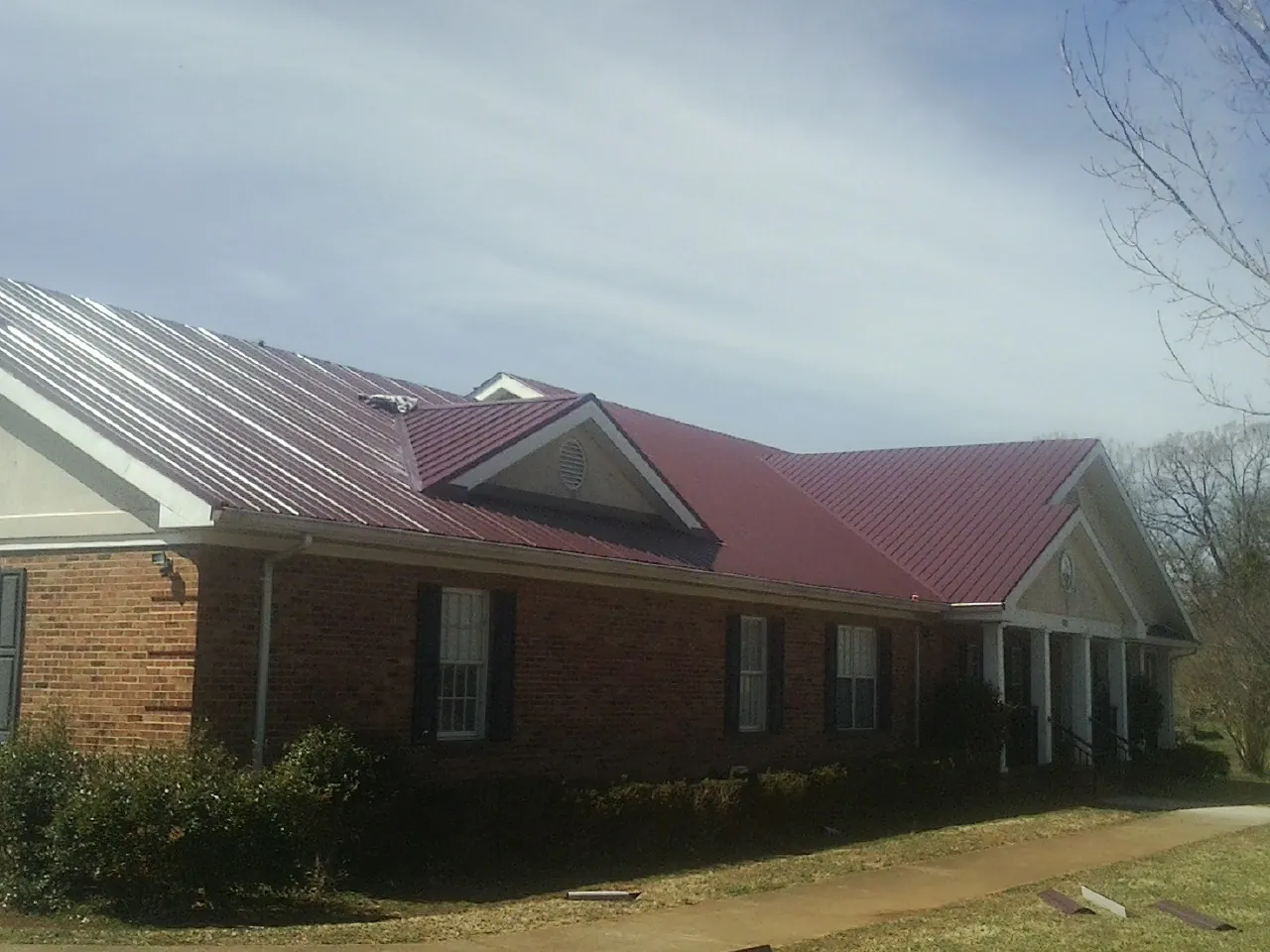 Red metal roof with gabled entries on a long brick building, from a Hail Damage Roof Repair job in Kenmore