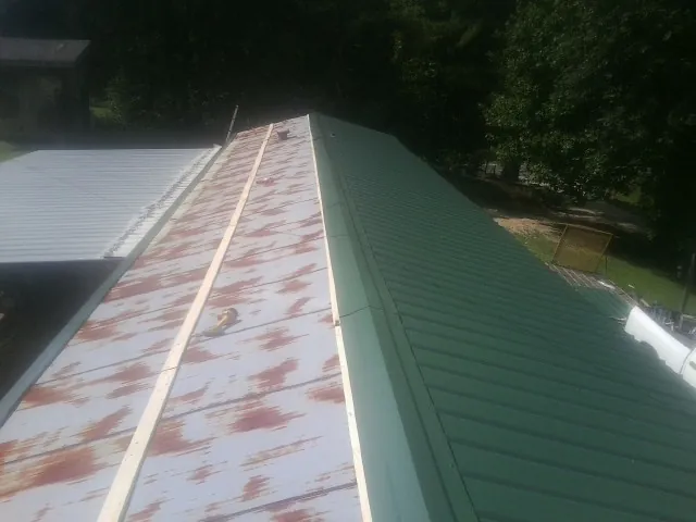 Old rusted panels beside newly installed green metal roofing — Wind Damage Roof Repair by Roofing Brothers in Kenmore