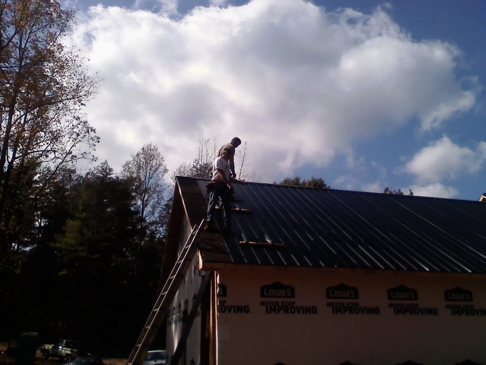 Roofer fastening dark metal panels high against a cloudy sky, from a Roof Inspection job in Kenmore